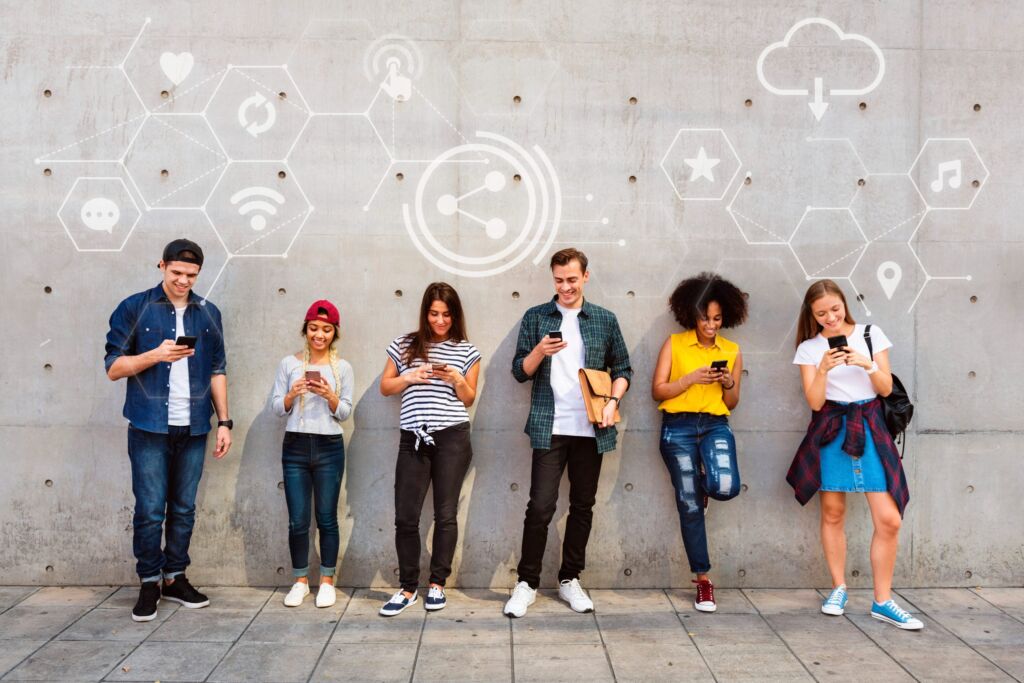 Vantagens do marketing de influ&ecirc;ncia : pessoas de diversas idades de p&eacute; em frente a uma parede interagindo com o celular