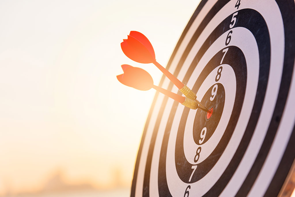 Campanha com nano influencer: como ter sucesso? : dardos fincados no centro de um alvo numerado e ao fundo claro de luzes