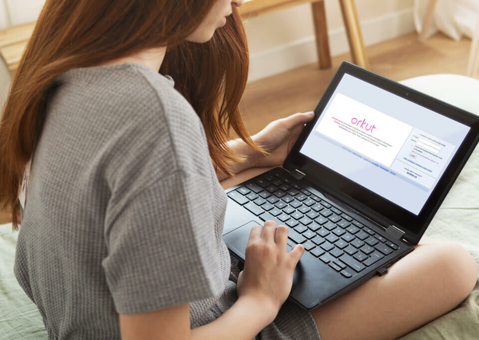 Garota sentada na cama com notebook aberto na tela do orkut
