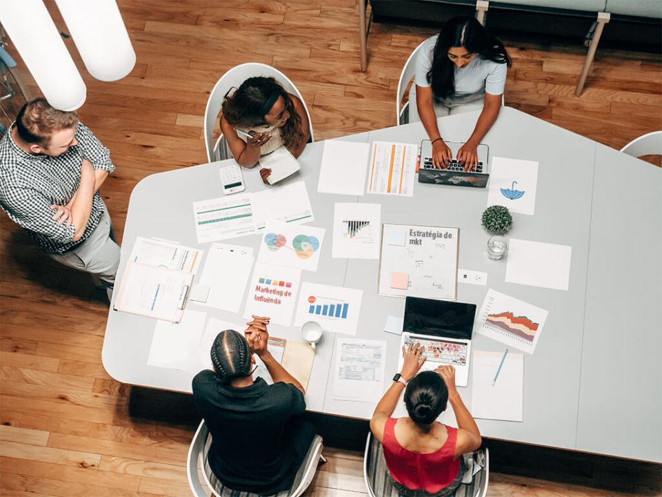 Equipe de agência de mkt de influência sentados ao entorno de uma mesa trabalhando em campanha
