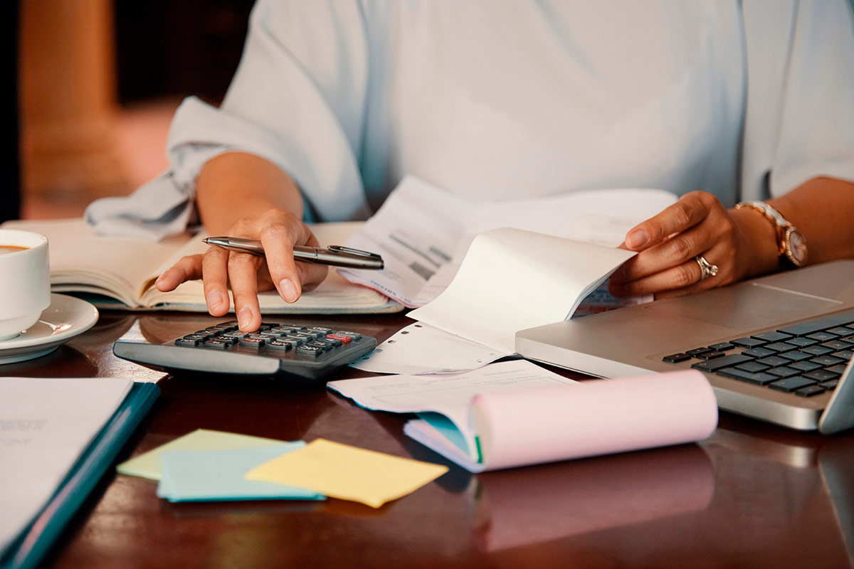 Uma pessoa em uma mesa, fazendo contas em uma calculadora e ao lado papeis e um computador, representando a defini&ccedil;&atilde;o de um or&ccedil;amento. Foto: &copy;Freepik