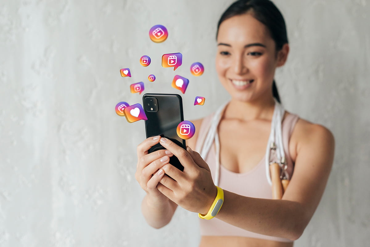 Influenciadora utilizando um celular e v&aacute;rios &iacute;cones de redes sociais saindo voando do aparelho, representando o benef&iacute;cios da gamifica&ccedil;&atilde;o que &eacute; o aumento de visibilidade. Foto: @Freepik.